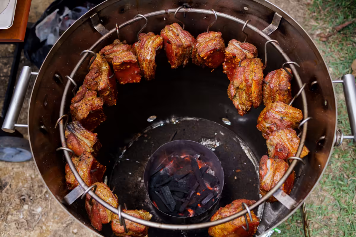 Asador de barril con costillas de cerdo colgadas sobre las brasas