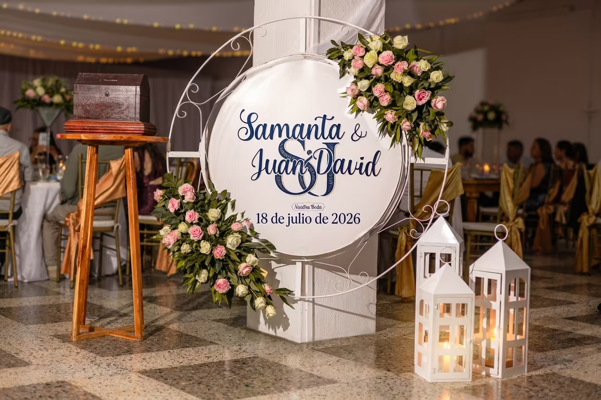 Cartel circular con los nombres de los novios enmarcado en un aro floral, junto a faroles blancos