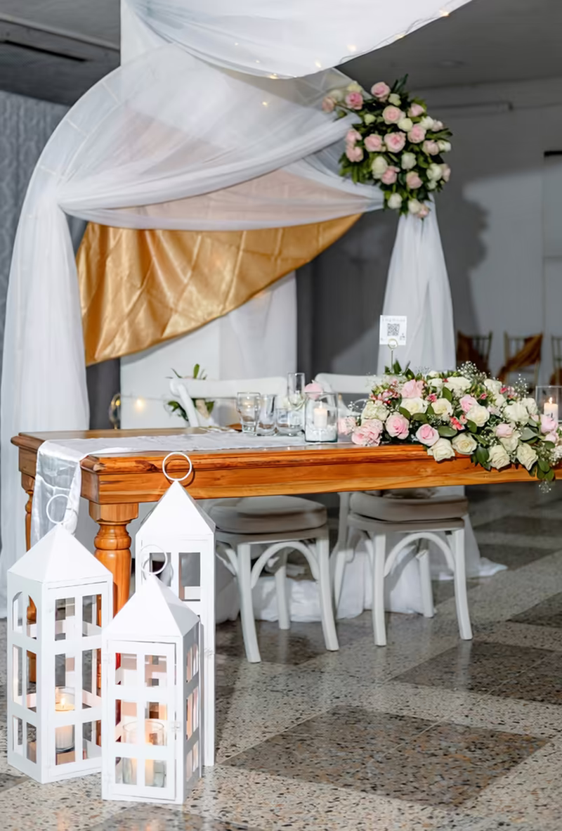 Mesa principal de los novios bajo un dosel de tela blanca y dorada, con arreglo floral y faroles