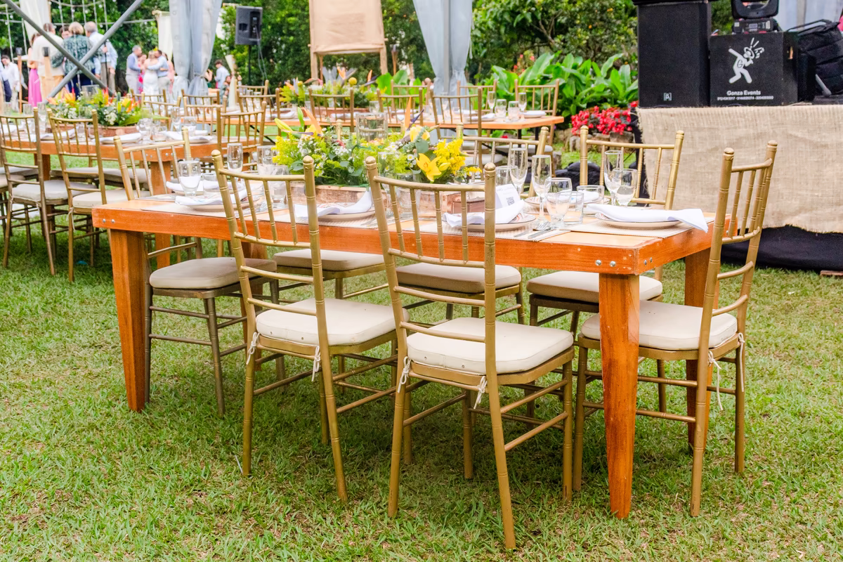 Mesa larga de madera con sillas doradas y flores amarillas sobre el césped