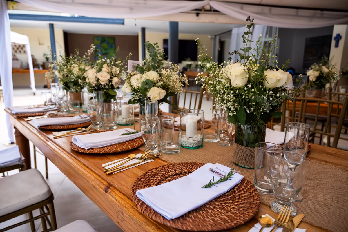 Mesa larga en interior con arreglos florales blancos altos y cristalería