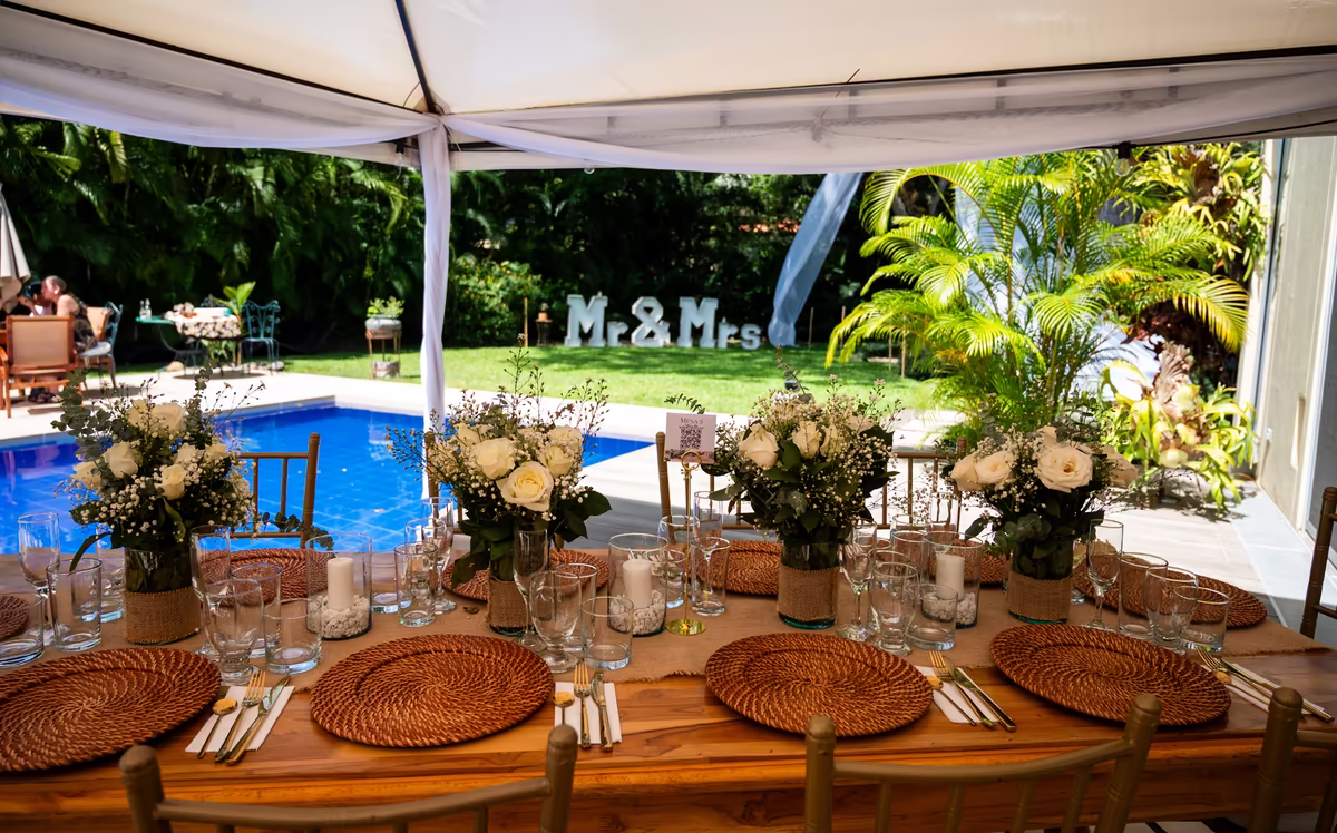 Mesa montada bajo carpa junto a la piscina para una boda