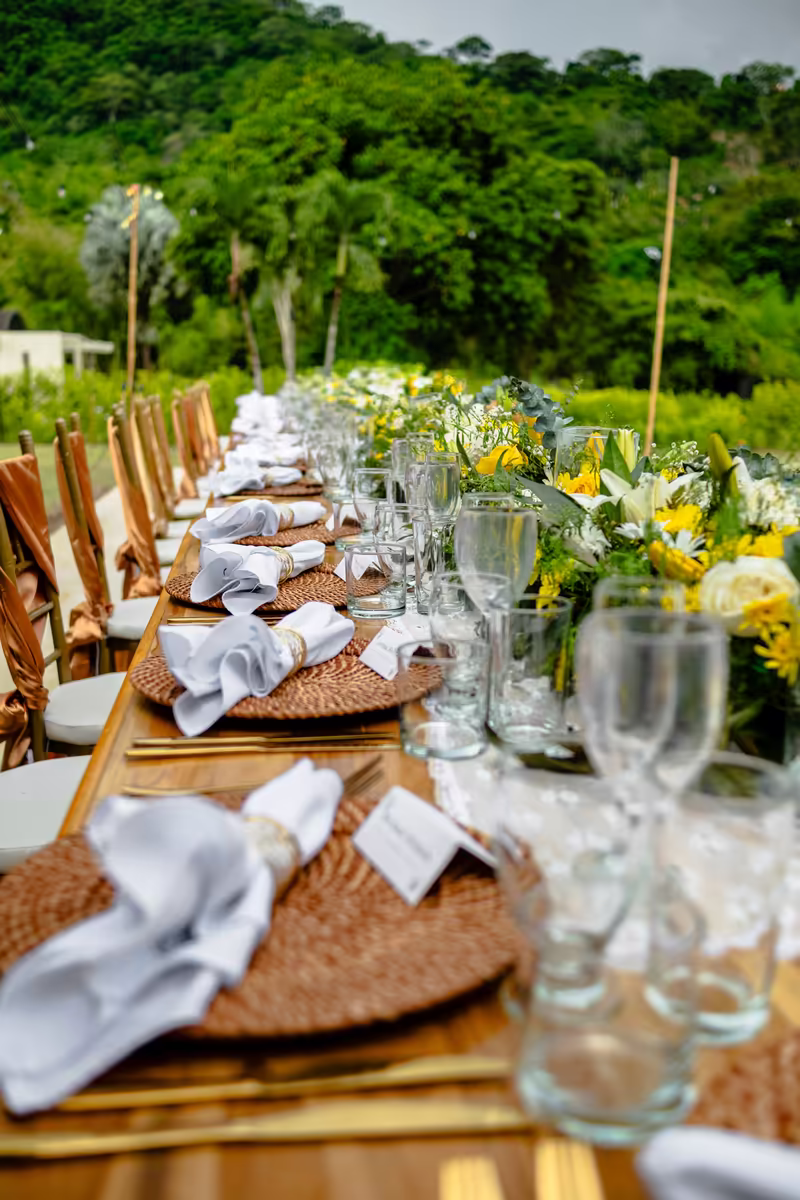 Mesa larga con flores amarillas y blancas y sillas de madera