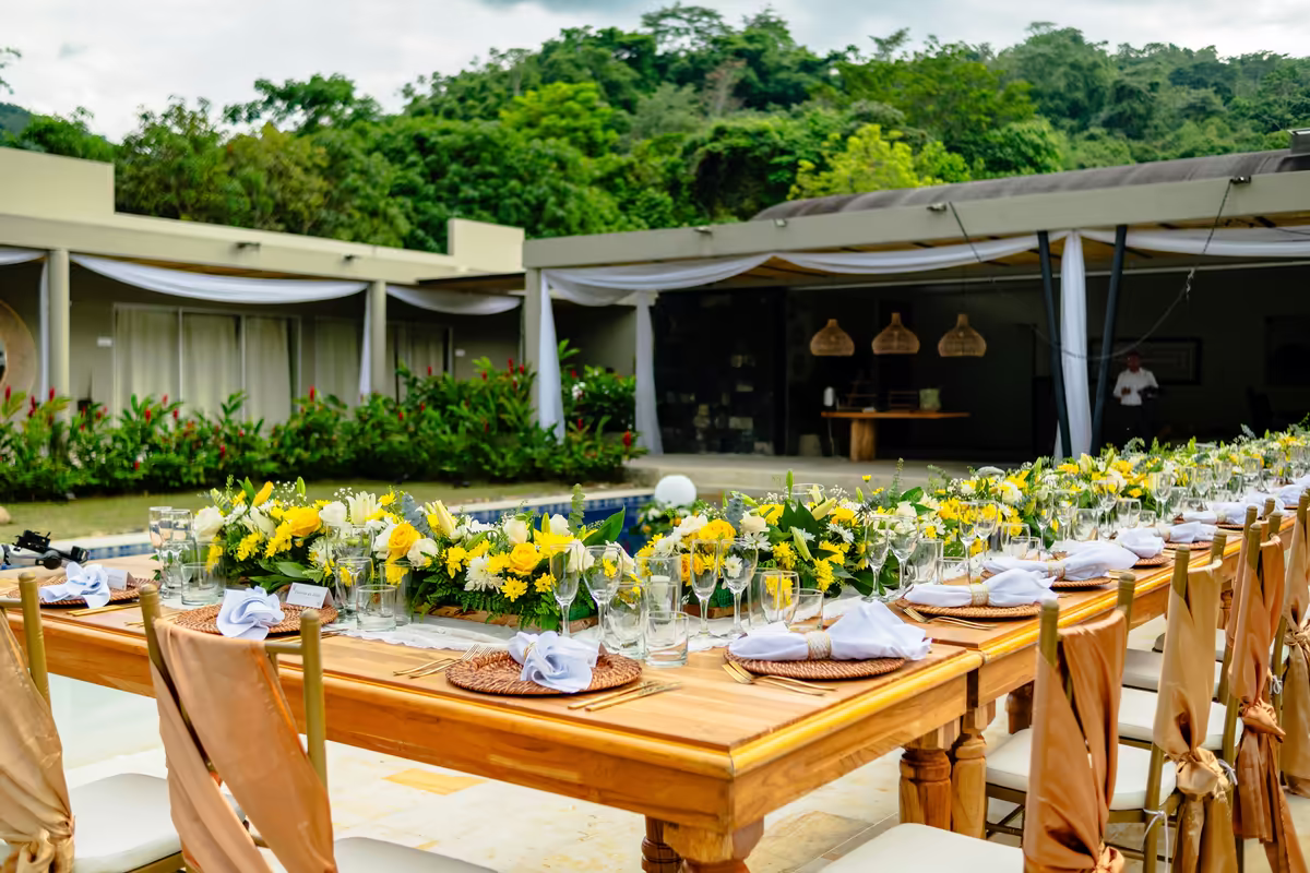 Mesa larga decorada con flores amarillas y blancas para una celebración al aire libre