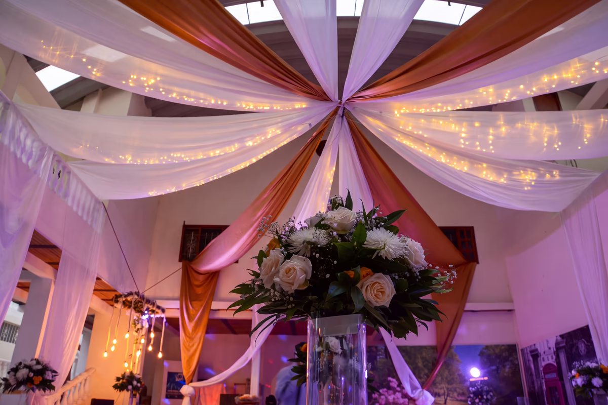 Techo del salón con telas recogidas en el centro y luces cálidas, sobre un centro floral