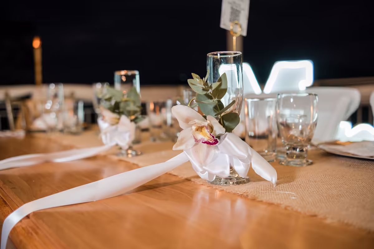 Detalle de mesa con camino de tela, cristalería y arreglo floral blanco