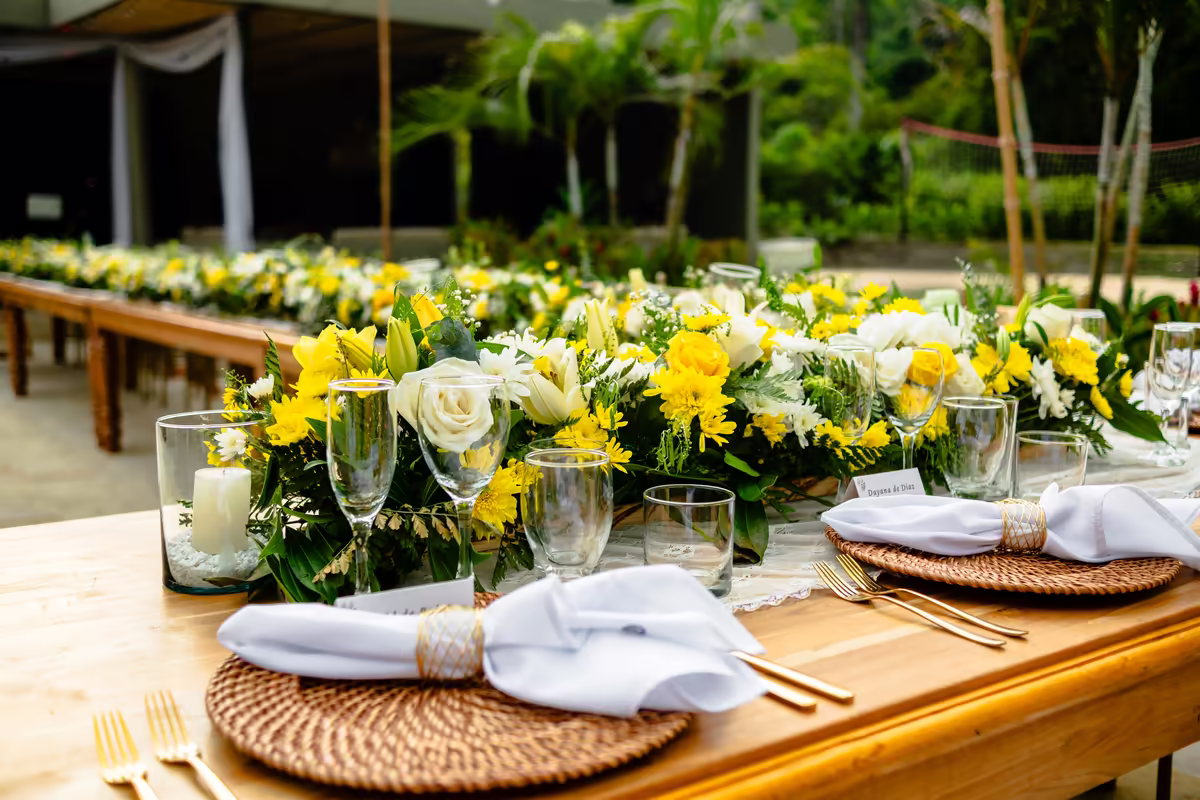 Centro de mesa con flores amarillas y blancas junto a la cristalería del puesto