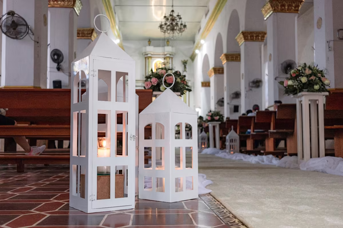 Pasillo central de la iglesia decorado con faroles blancos y arreglos florales sobre pedestales
