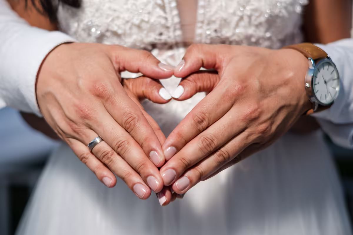 Manos de los novios formando un corazón, con los anillos de matrimonio a la vista