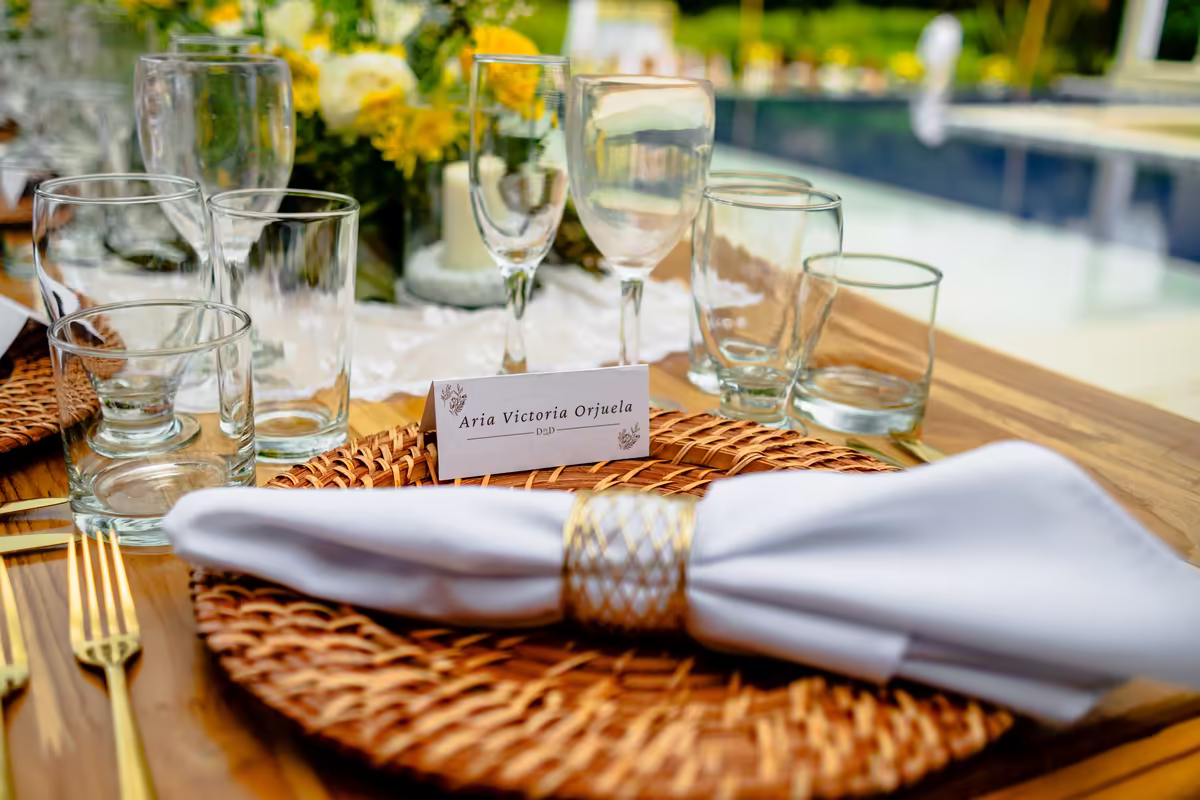 Puesto de mesa con plato, servilleta y tarjeta con el nombre del invitado, junto a la piscina