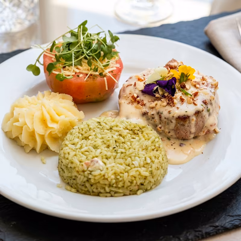 Medallón con salsa cremosa y frutos secos, acompañado de arroz verde, puré y tomate relleno