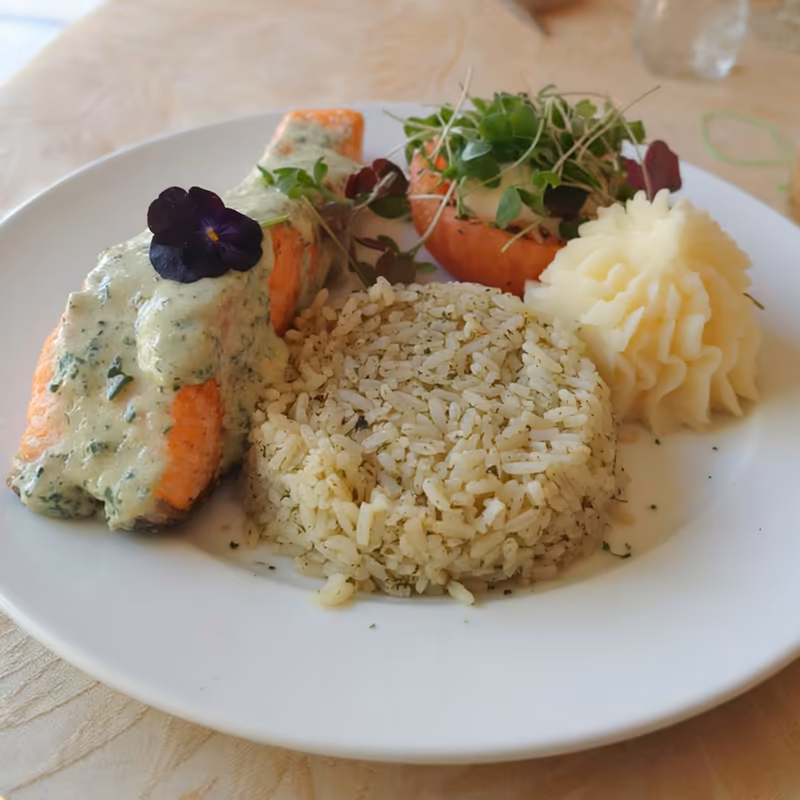 Porción de salmón bañada en salsa de hierbas, con arroz y puré de papa
