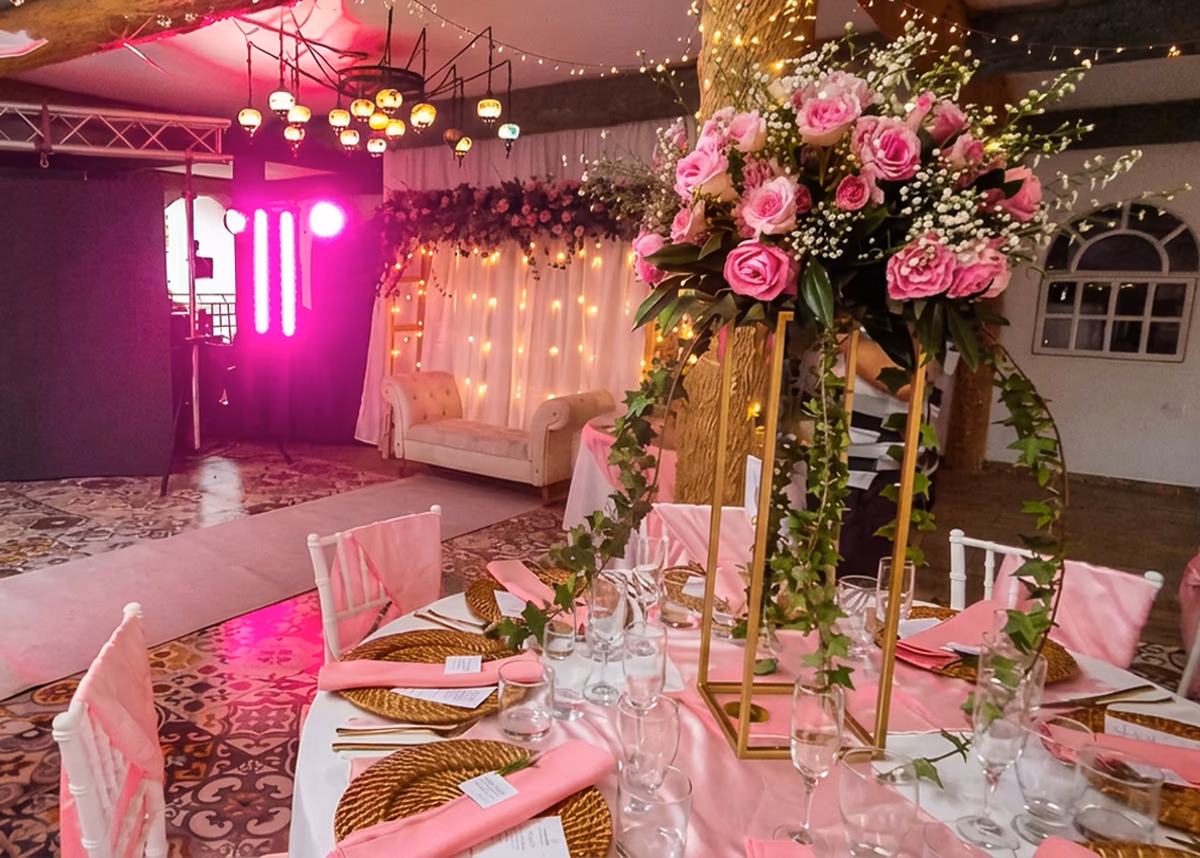 Salón de quince años iluminado en rosa, con centro floral alto y mesa larga vestida de rosa